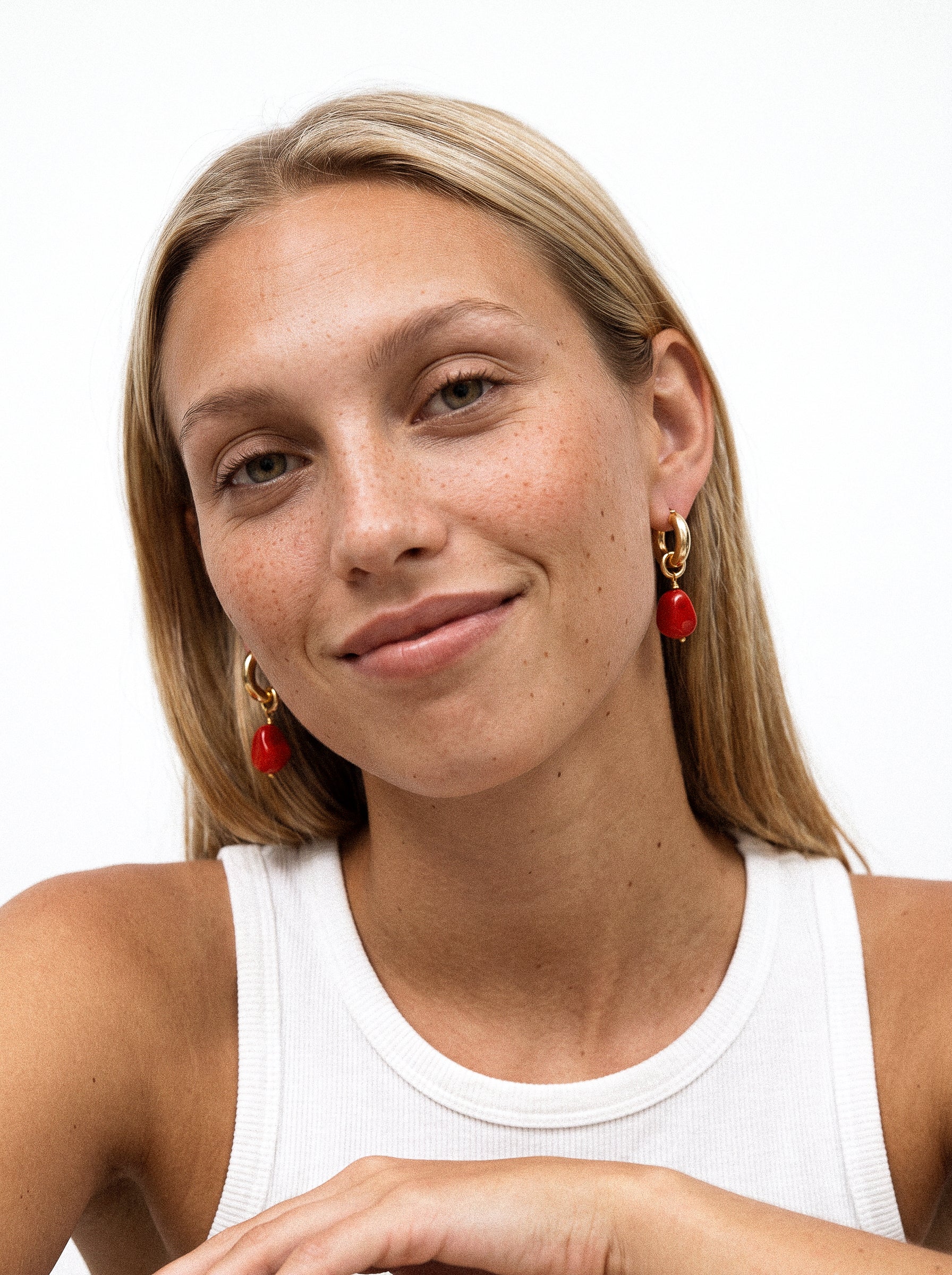 Pozłacane kolczyki z czerowoną zawieszką na modelce.