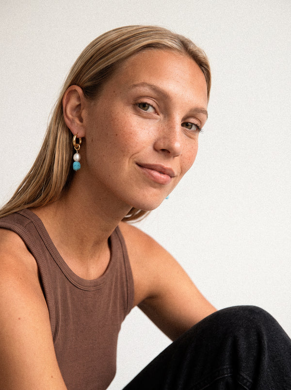 Pozłacany kolczyk z niebieską i białą zawieszką na modelce.