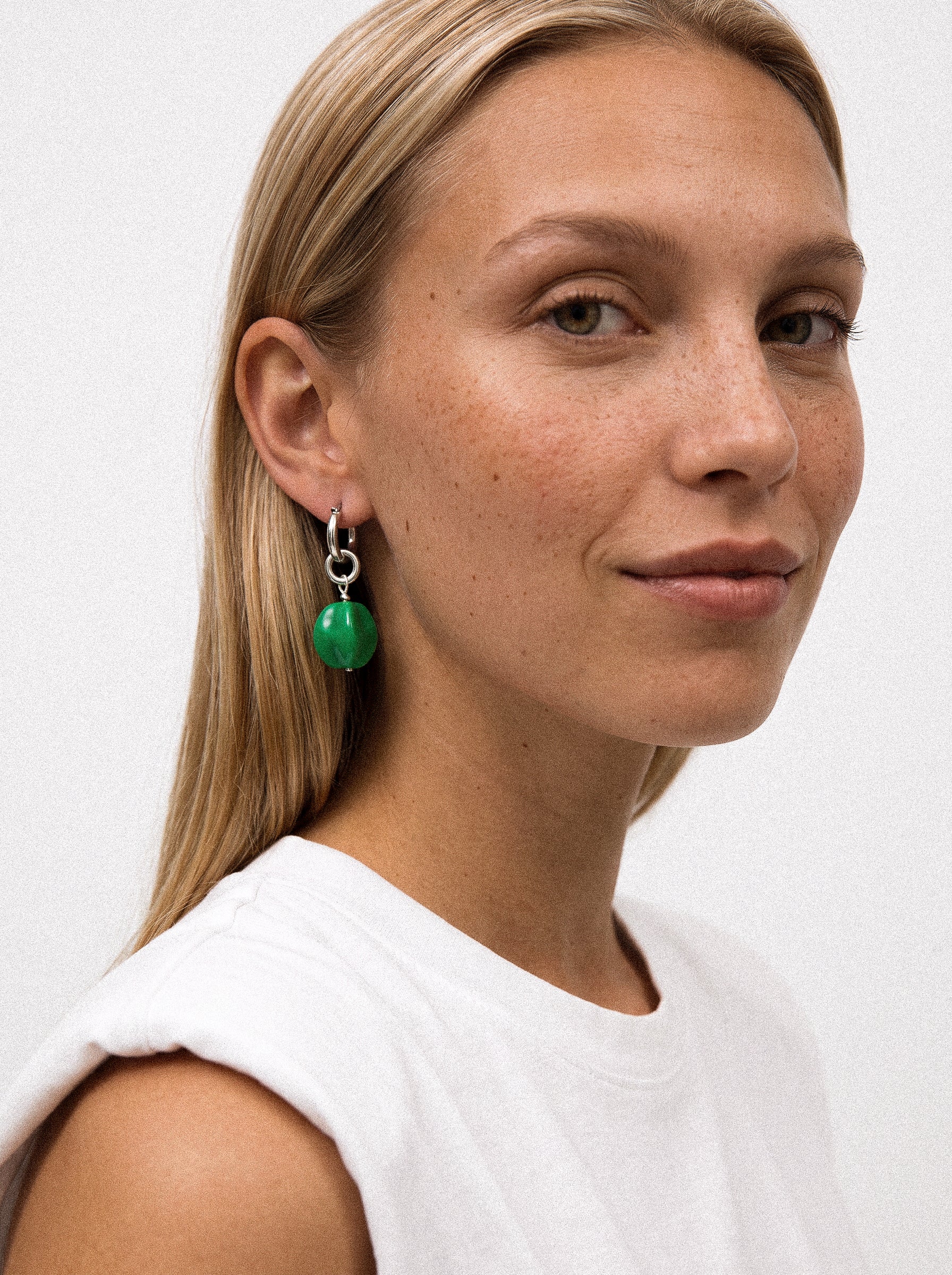 Srebrny kolczyk z zieloną zawieszką na modelce.