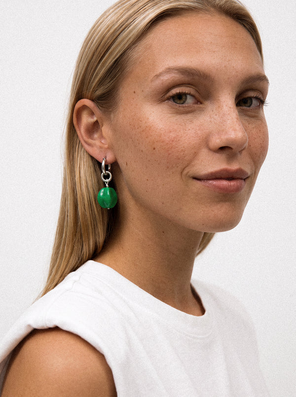 Srebrny kolczyk z zieloną zawieszką na modelce.