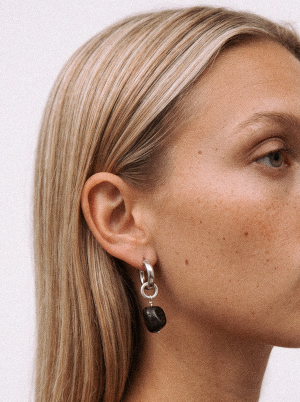 Srebrny kolczyk z czarną zawieszką z żywicy na modelce. 